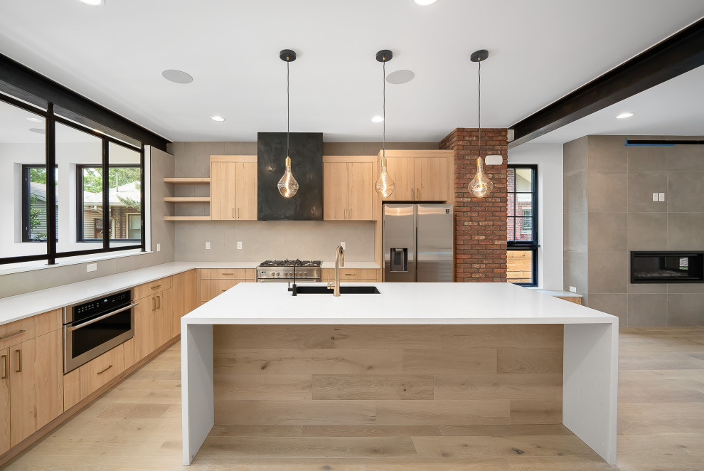 Design ideas for a small industrial open plan kitchen in Denver with a submerged sink, flat-panel cabinets, light wood cabinets, engineered stone countertops, grey splashback, ceramic splashback, stainless steel appliances, light hardwood flooring, an island, brown floors, white worktops and exposed beams.