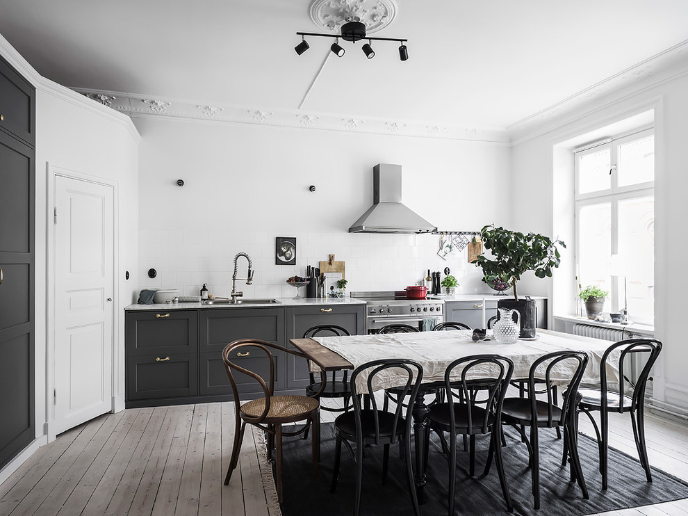 Minimalistisk inredning av ett kök och matrum, med luckor med infälld panel, grå skåp och vitt stänkskydd