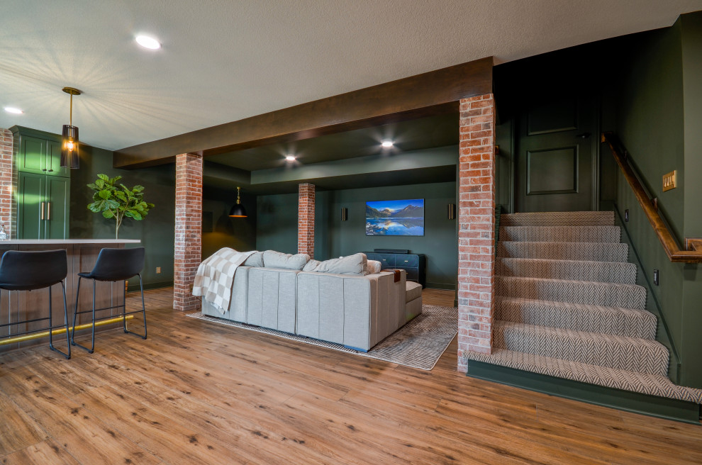 Photo of a large modern walk-out basement in Kansas City with a home bar, green walls, vinyl floors, exposed beam and brick walls.