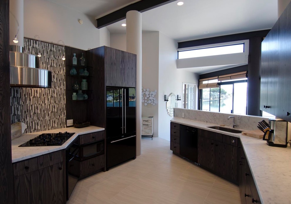 Photo of a mid-sized beach style galley kitchen in San Francisco with a drop-in sink, flat-panel cabinets, dark wood cabinets, multi-coloured splashback, matchstick tile splashback, black appliances and ceramic floors.