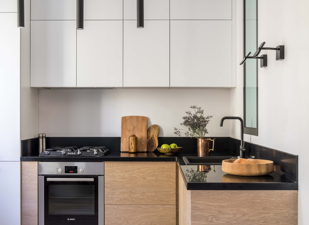 Small scandinavian l-shaped open plan kitchen in Moscow with flat-panel cabinets, white cabinets, black splashback, stainless steel appliances, no island, black benchtop, solid surface benchtops, stone slab splashback and a drop-in sink.