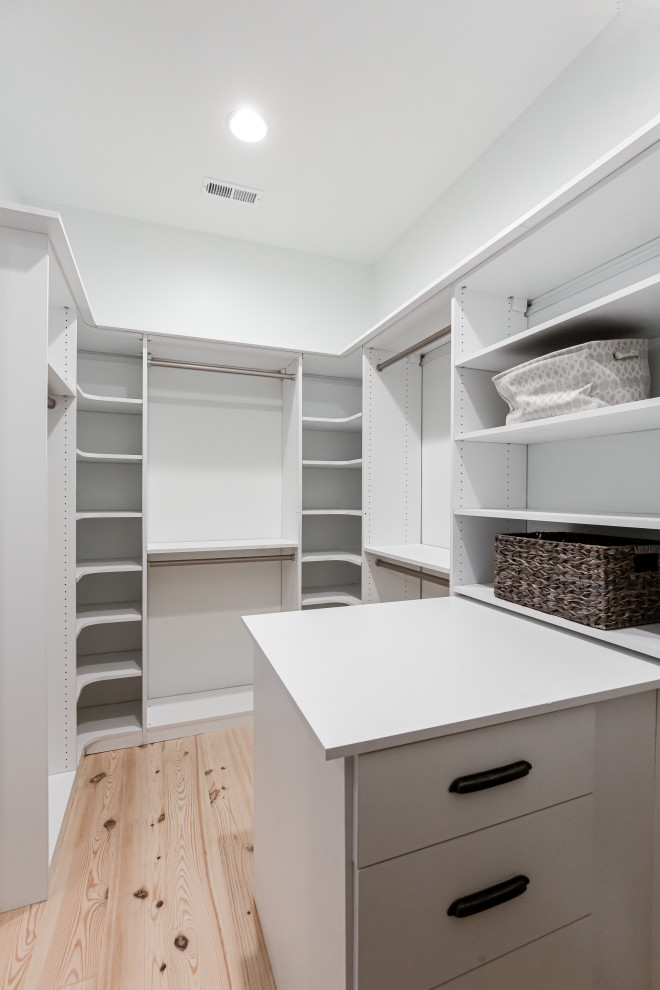 Ejemplo de armario vestidor actual pequeño con armarios con paneles lisos, puertas de armario blancas, suelo de madera clara y suelo beige