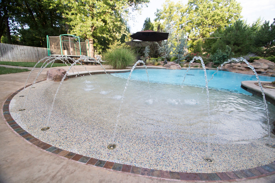 This is an example of a large modern backyard custom-shaped natural pool in Other with a water feature.