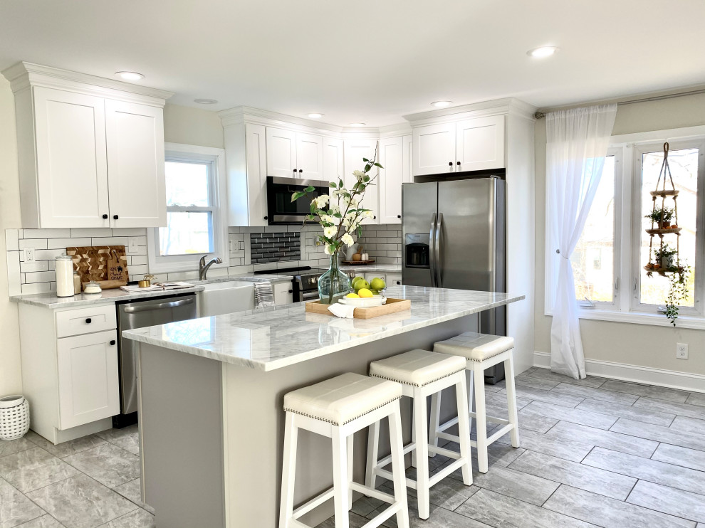 Mid-sized transitional l-shaped ceramic tile and gray floor enclosed kitchen photo with a farmhouse sink, recessed-panel cabinets, white cabinets, granite countertops, white backsplash, cement tile backsplash, stainless steel appliances, an island and gray countertops