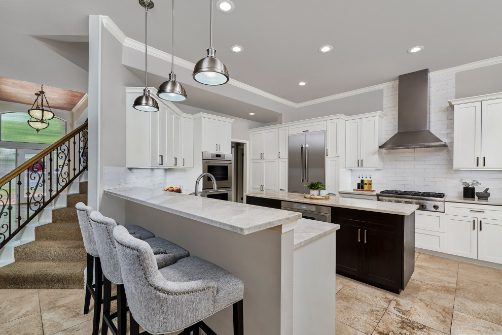 Example of a transitional u-shaped porcelain tile and beige floor kitchen pantry design with shaker cabinets, white cabinets, quartzite countertops, white backsplash, porcelain backsplash, stainless steel appliances, an island and beige countertops