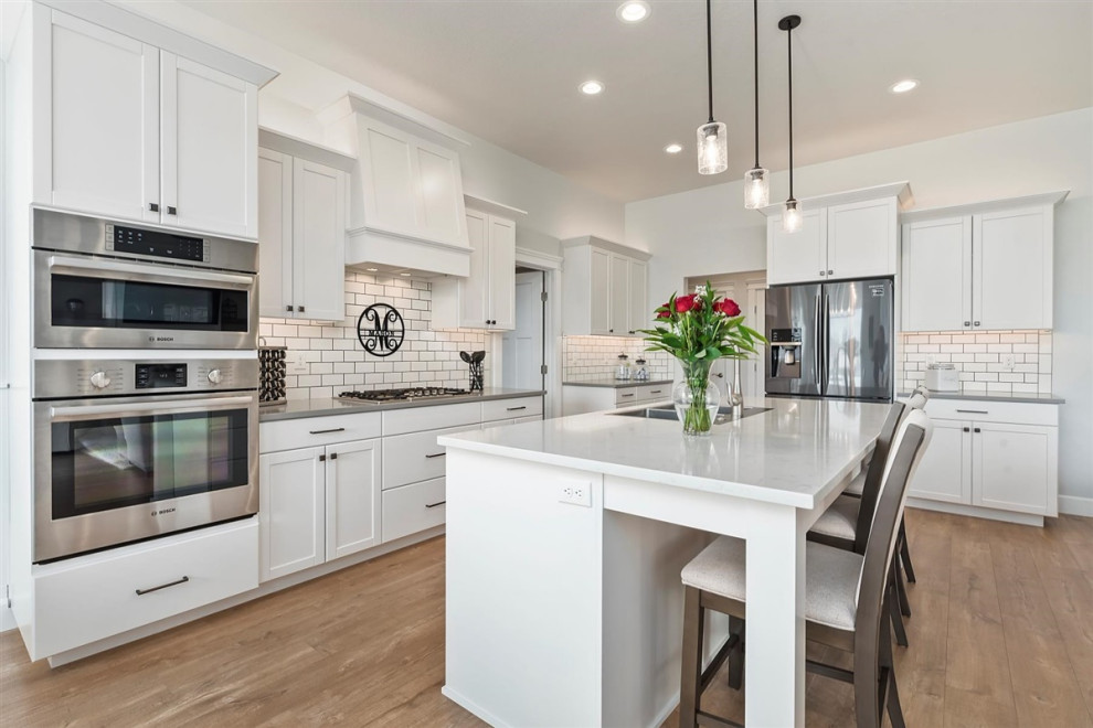 Photo of a mid-sized traditional l-shaped eat-in kitchen in Boise with a drop-in sink, recessed-panel cabinets, white cabinets, wood benchtops, white splashback, subway tile splashback, stainless steel appliances, laminate floors, with island, brown floor and multi-coloured benchtop.