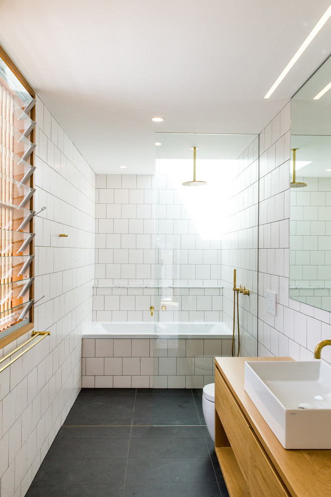 Contemporary master bathroom in Sydney with flat-panel cabinets, medium wood cabinets, an alcove tub, a curbless shower, a one-piece toilet, white tile, white walls, a vessel sink, wood benchtops, black floor, an open shower, concrete floors and brown benchtops.