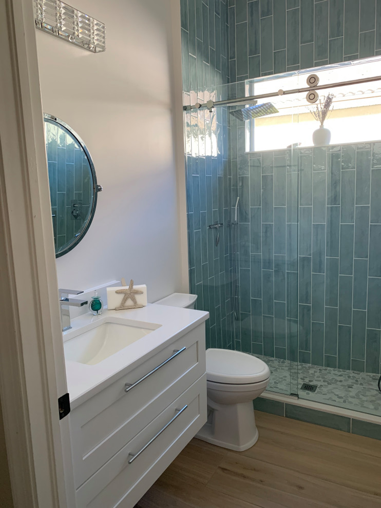 Пример оригинального дизайна: маленькая ванная комната в морском стиле с фасадами в стиле шейкер, белыми фасадами, душем в нише, раздельным унитазом, синей плиткой, плиткой кабанчик, белыми стенами, полом из керамогранита, душевой кабиной, врезной раковиной, столешницей из искусственного кварца, разноцветным полом, душем с раздвижными дверями, белой столешницей, тумбой под одну раковину и подвесной тумбой для на участке и в саду