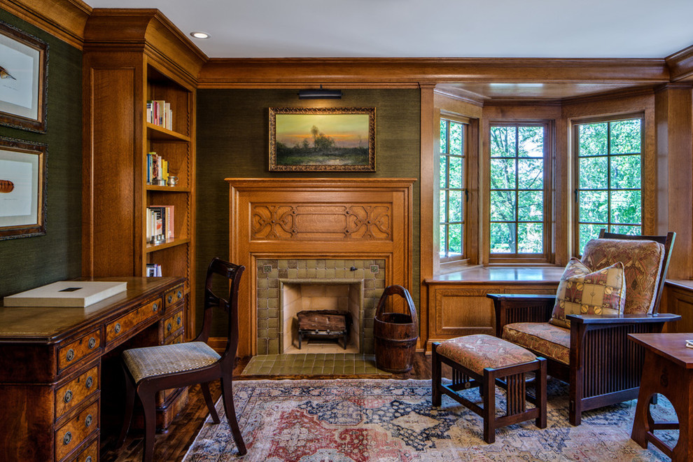 This is an example of an arts and crafts home office in Minneapolis with green walls, dark hardwood floors, a standard fireplace, a tile fireplace surround, a freestanding desk and brown floor.