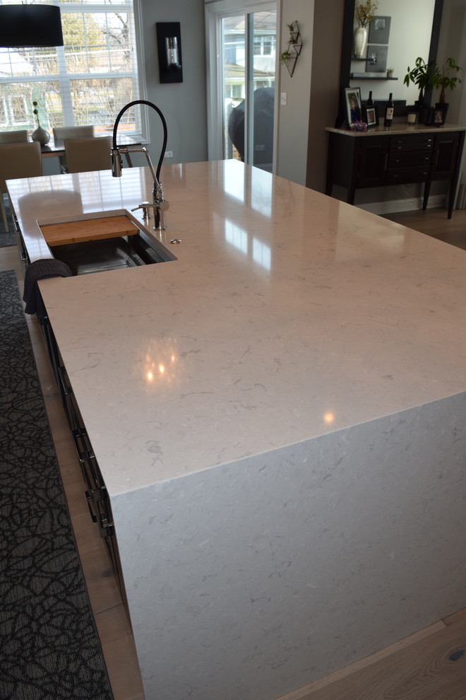 Example of a large transitional l-shaped light wood floor and multicolored floor eat-in kitchen design in Chicago with beaded inset cabinets, white cabinets, quartz countertops, black backsplash, ceramic backsplash, stainless steel appliances and an island
