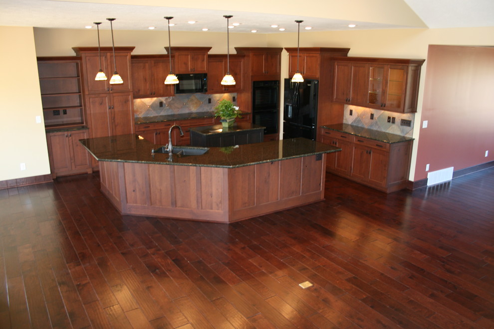This is an example of a large traditional l-shaped open plan kitchen in Omaha with a double-bowl sink, recessed-panel cabinets, dark wood cabinets, granite benchtops, beige splashback, ceramic splashback, black appliances, dark hardwood floors, multiple islands and blue floor.