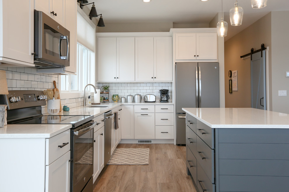 Inspiration for a large transitional u-shaped light wood floor and brown floor eat-in kitchen remodel with an undermount sink, recessed-panel cabinets, white cabinets, quartz countertops, white backsplash, subway tile backsplash, stainless steel appliances, an island and white countertops