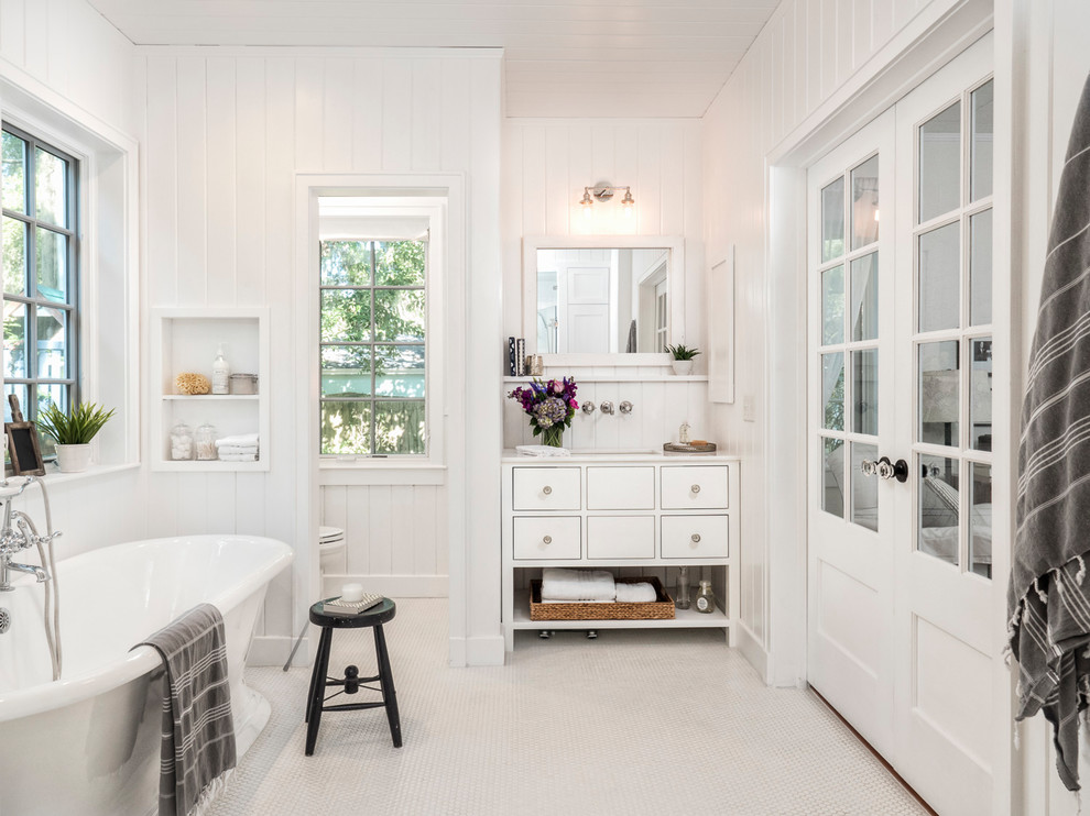 Inspiration for a mid-sized country master bathroom with flat-panel cabinets, white cabinets, a freestanding tub, a two-piece toilet, white tile, white walls, mosaic tile floors, an undermount sink, engineered quartz benchtops, white floor and an enclosed toilet.