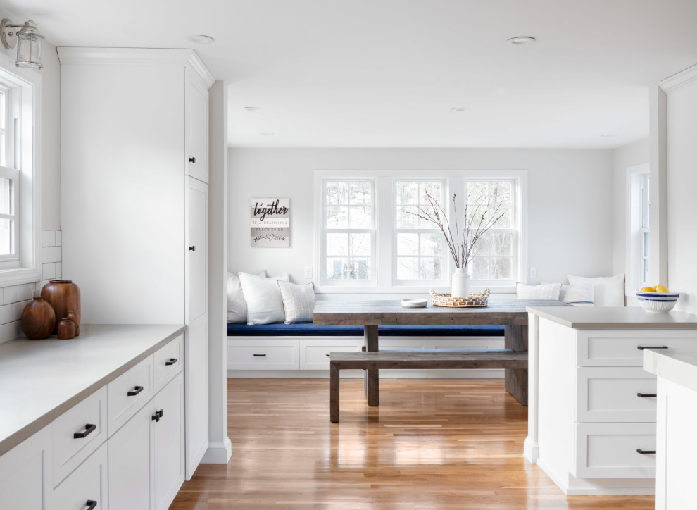 Photo of a mid-sized transitional u-shaped eat-in kitchen in Boston with an undermount sink, shaker cabinets, white cabinets, quartz benchtops, white splashback, subway tile splashback, stainless steel appliances, light hardwood floors, with island, beige floor and grey benchtop.