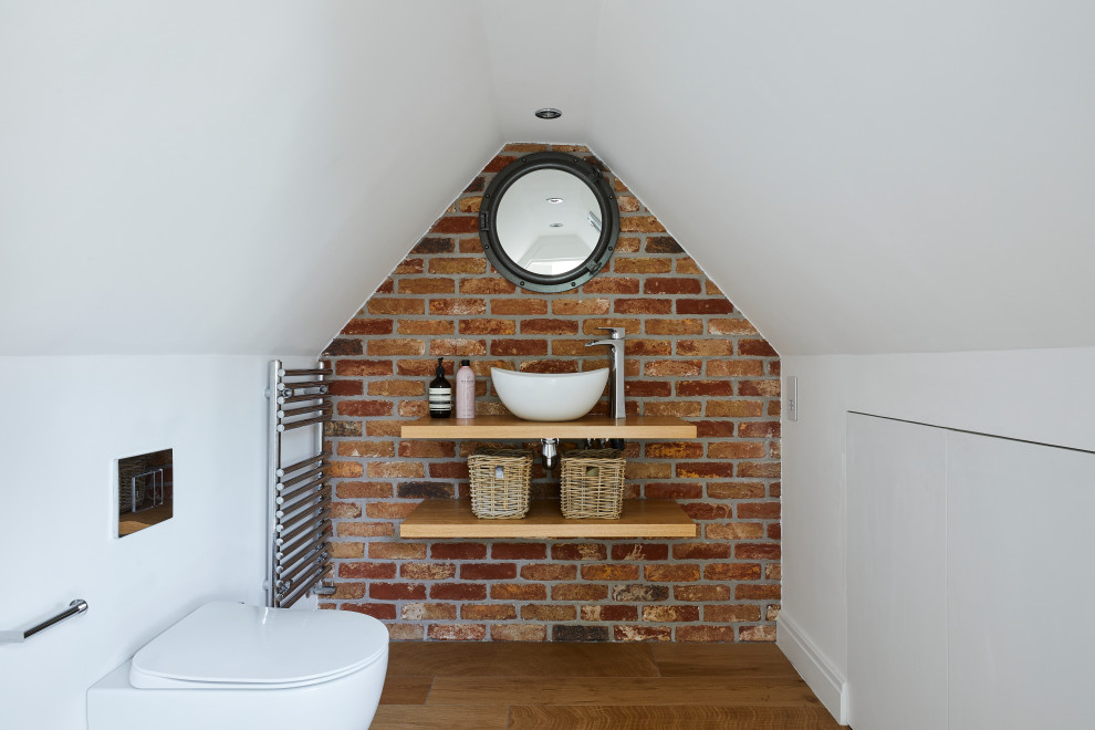 Photo of a mid-sized transitional bathroom in London with white walls, vaulted, medium hardwood floors, a vessel sink, wood benchtops, brown floor, beige benchtops, a single vanity and brick walls.