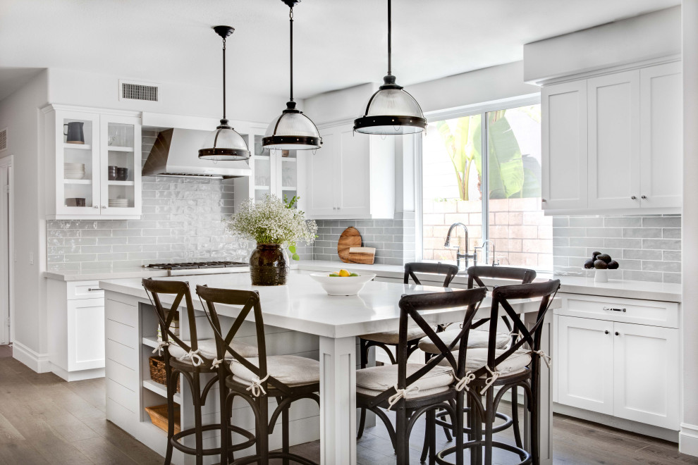 Transitional l-shaped dark wood floor and brown floor eat-in kitchen photo in Orange County with an island, stainless steel appliances, an undermount sink, shaker cabinets, white cabinets, gray backsplash, subway tile backsplash and white countertops