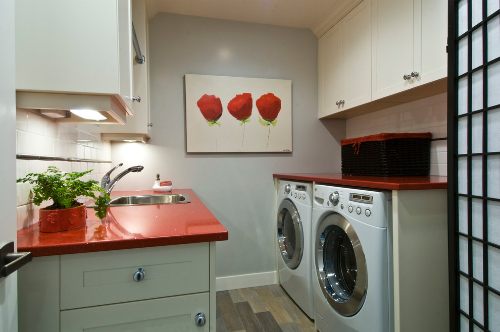 Photo of a mid-sized traditional galley dedicated laundry room in Vancouver with a drop-in sink, shaker cabinets, white cabinets, quartz benchtops, grey walls, porcelain floors, a side-by-side washer and dryer and red benchtop.