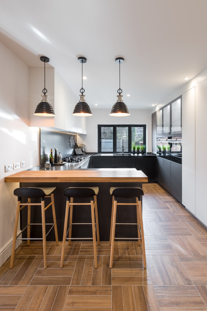 Mid-sized contemporary u-shaped kitchen in Gloucestershire with grey cabinets, quartzite benchtops, grey splashback, black appliances, porcelain floors, a peninsula, brown floor and flat-panel cabinets.