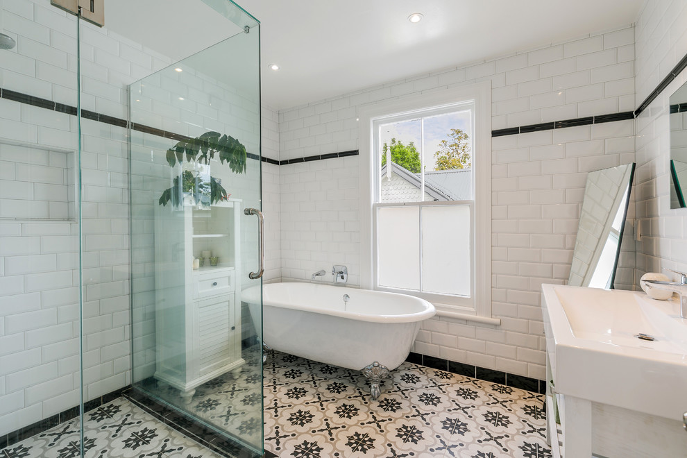 This is an example of a transitional 3/4 bathroom in Auckland with shaker cabinets, white cabinets, a claw-foot tub, a corner shower, black and white tile, subway tile, a console sink, multi-coloured floor and a hinged shower door.