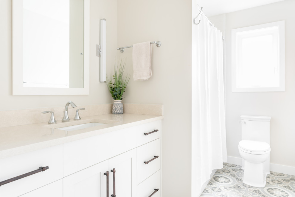 This is an example of a small country 3/4 bathroom in Vancouver with shaker cabinets, white cabinets, an alcove tub, an alcove shower, a two-piece toilet, white tile, ceramic tile, beige walls, porcelain floors, an undermount sink, engineered quartz benchtops, grey floor, a shower curtain and beige benchtops.