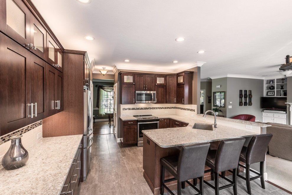 Inspiration for a mid-sized transitional u-shaped vinyl floor and brown floor kitchen remodel with an undermount sink, recessed-panel cabinets, brown cabinets, quartz countertops, multicolored backsplash, porcelain backsplash, stainless steel appliances, a peninsula and multicolored countertops