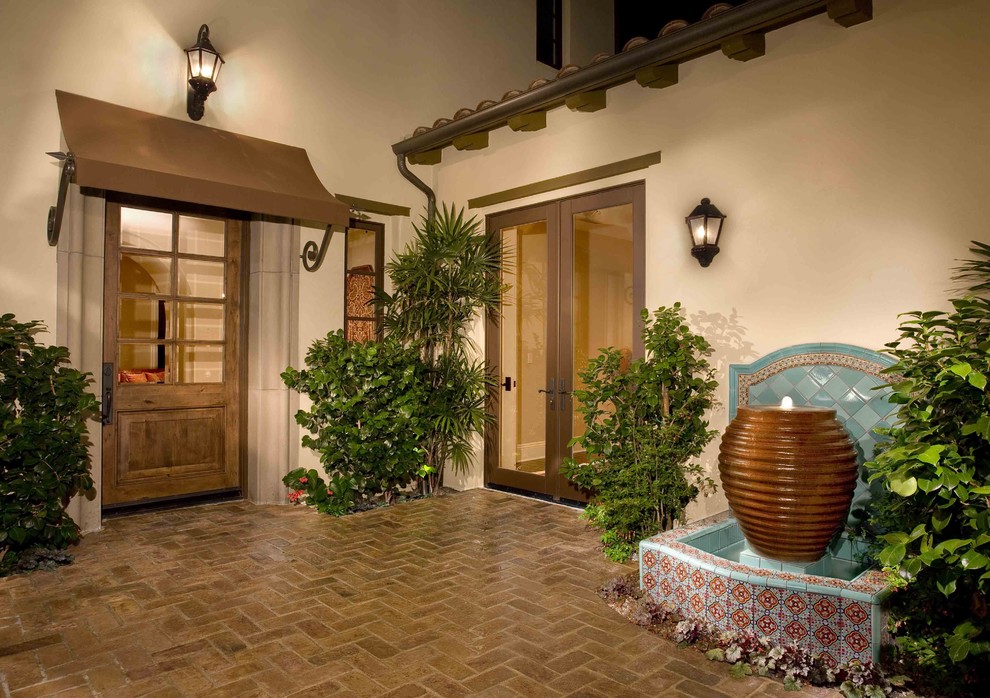 This is an example of a large mediterranean courtyard patio in Orange County with a water feature and brick pavers.