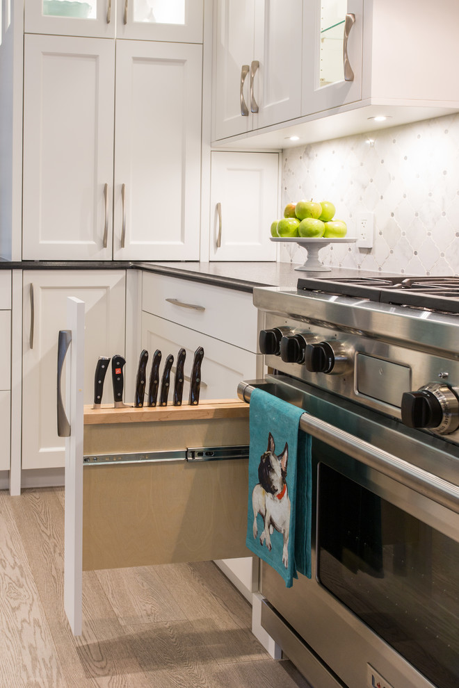Example of a large transitional l-shaped medium tone wood floor and beige floor eat-in kitchen design in Vancouver with an undermount sink, shaker cabinets, white cabinets, granite countertops, gray backsplash, marble backsplash, stainless steel appliances, an island and black countertops
