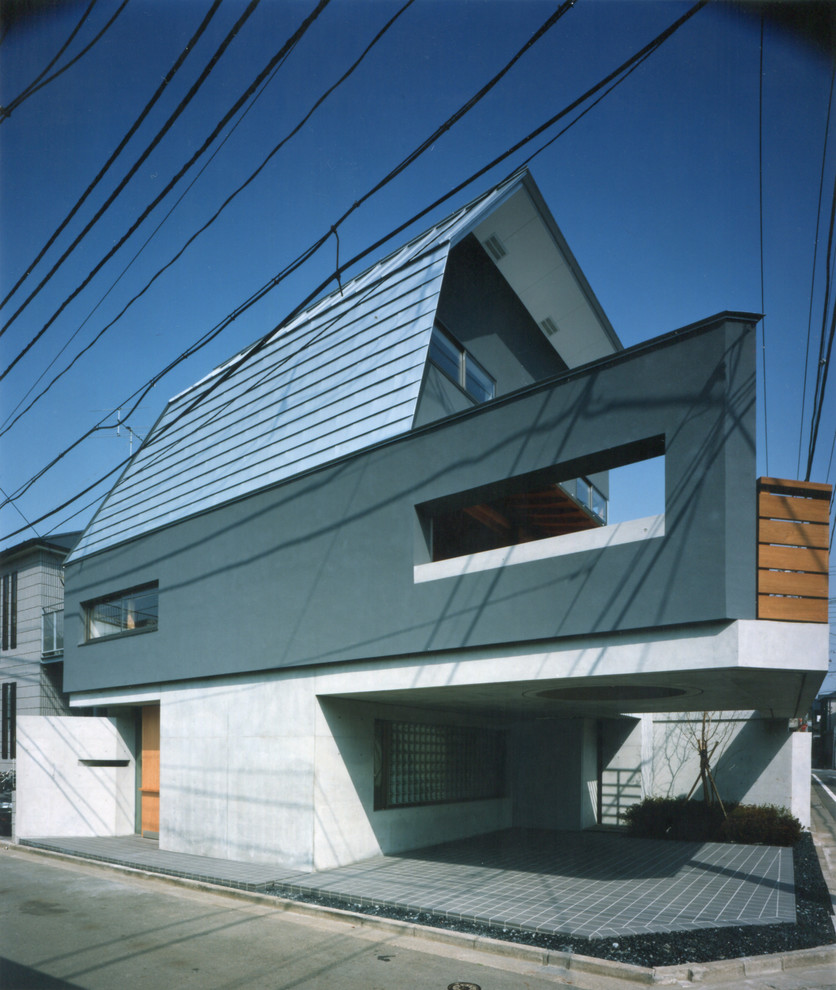 Mid-sized asian three-storey stucco grey house exterior in Tokyo with a shed roof and a metal roof.