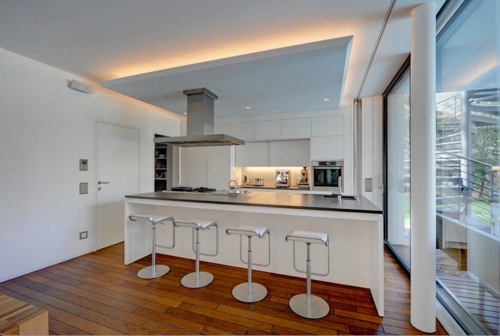 Inspiration for a large contemporary open plan kitchen in Munich with flat-panel cabinets, white cabinets, white splashback, stainless steel appliances, dark hardwood floors, with island and a single-bowl sink.