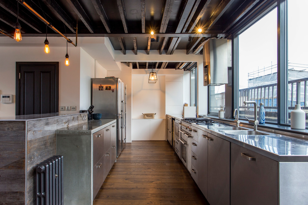 Inspiration for a mid-sized industrial galley kitchen in London with a double-bowl sink, flat-panel cabinets, stainless steel cabinets, stainless steel benchtops, stainless steel appliances, dark hardwood floors, brown floor, grey benchtop and no island.