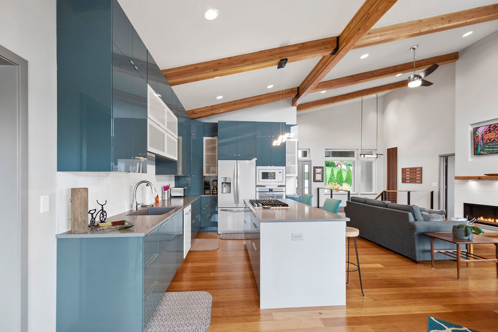 This is an example of a large contemporary l-shaped open plan kitchen in Kansas City with an undermount sink, flat-panel cabinets, turquoise cabinets, quartz benchtops, white splashback, porcelain splashback, white appliances, light hardwood floors, with island, brown floor and grey benchtop.