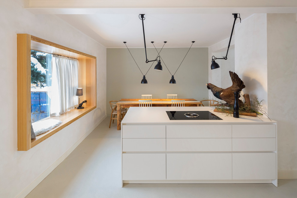 This is an example of a mid-sized scandinavian galley open plan kitchen in Berlin with an integrated sink, flat-panel cabinets, white cabinets, beige splashback, subway tile splashback, black appliances, with island, white floor and white benchtop.