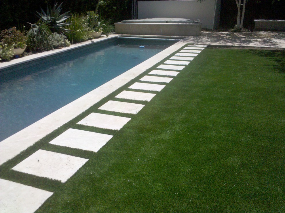 This is an example of a mid-sized modern backyard rectangular lap pool in Los Angeles with natural stone pavers and a hot tub.