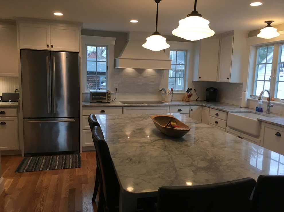 Transitional l-shaped medium tone wood floor eat-in kitchen photo in Boston with a farmhouse sink, shaker cabinets, white cabinets, white backsplash, porcelain backsplash, stainless steel appliances and an island