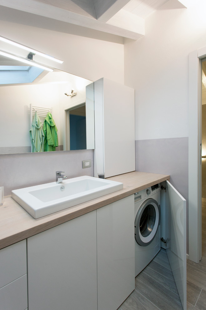 Photo of a mid-sized modern bathroom in Milan with flat-panel cabinets, white cabinets, wood benchtops, grey walls, porcelain floors, a trough sink, beige benchtops and a laundry.