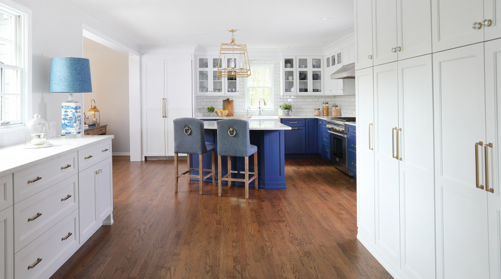 Example of a large transitional l-shaped medium tone wood floor and brown floor eat-in kitchen design in Chicago with an island, a farmhouse sink, beaded inset cabinets, quartz countertops, white backsplash, glass tile backsplash, paneled appliances, white countertops and white cabinets