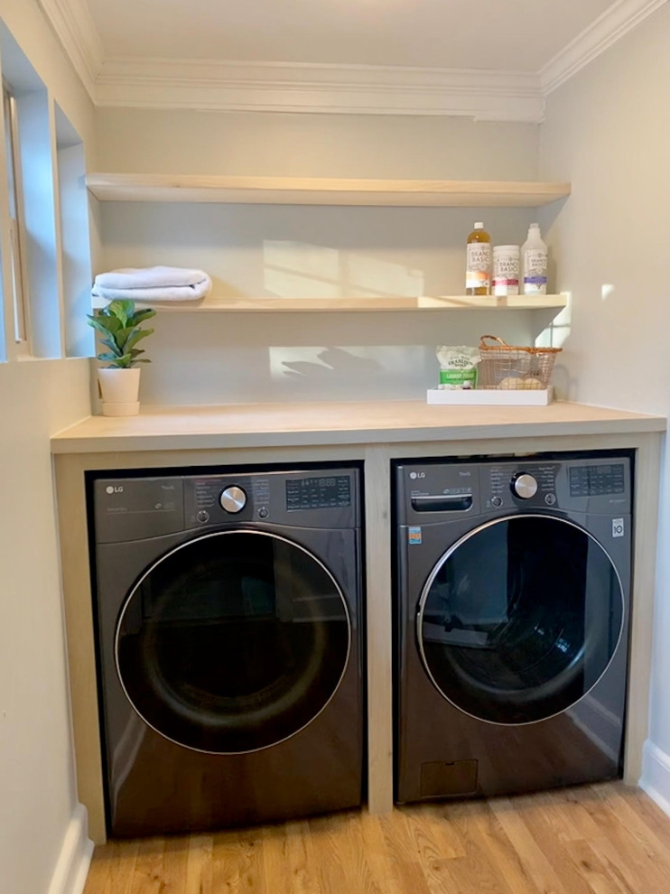 Ejemplo de cuarto de lavado lineal con armarios abiertos, puertas de armario de madera clara, encimera de madera y lavadora y secadora escondidas