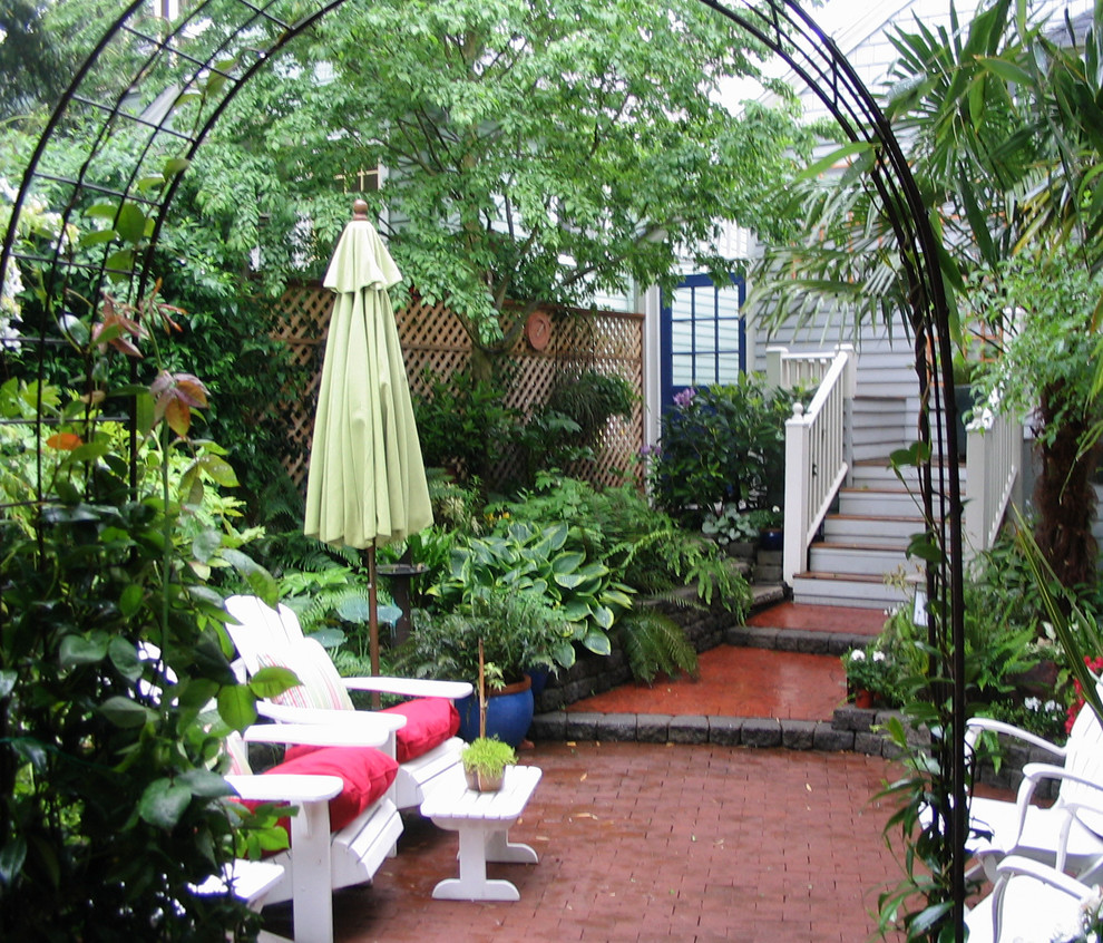 Small tropical backyard shaded garden in Seattle with a retaining wall and brick pavers for summer.