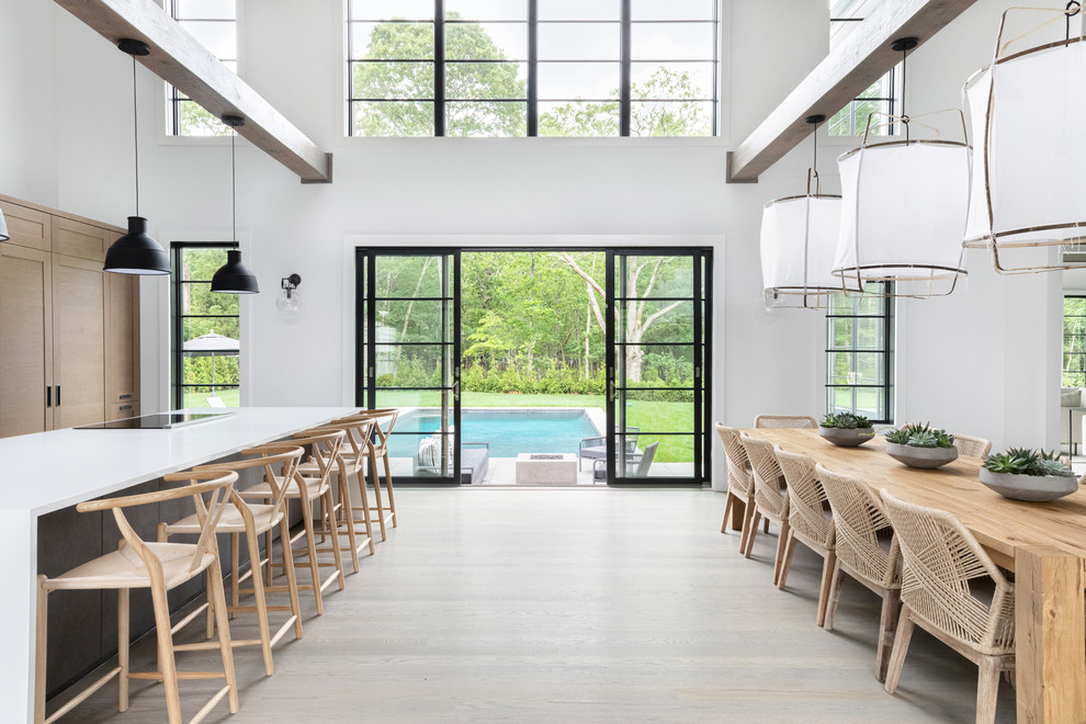 This is an example of a large beach style single-wall eat-in kitchen in New York with medium wood cabinets, marble benchtops, grey splashback, black appliances, dark hardwood floors, with island, grey floor and white benchtop.