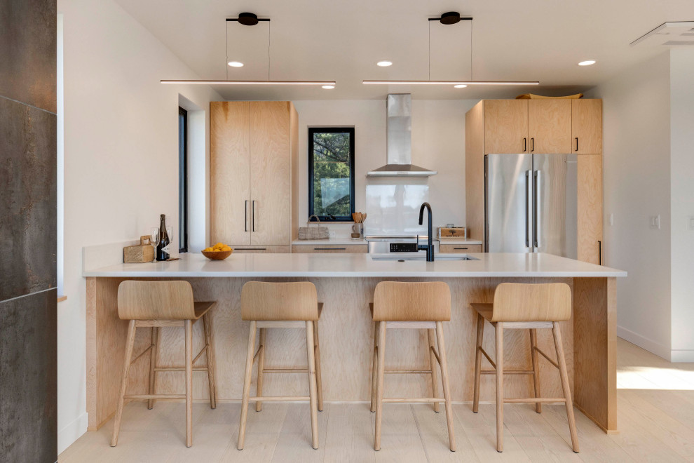 This is an example of a beach style galley kitchen in Portland with an undermount sink, flat-panel cabinets, light wood cabinets, white splashback, stainless steel appliances, light hardwood floors, a peninsula, beige floor and white benchtop.