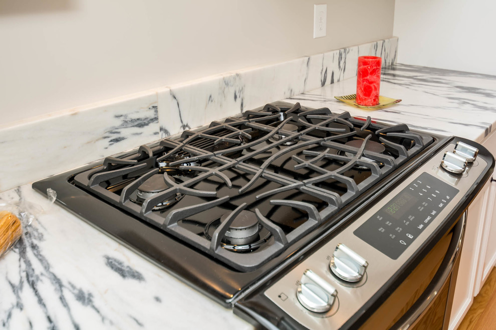 Example of a large transitional l-shaped brown floor and medium tone wood floor eat-in kitchen design in Boston with an undermount sink, recessed-panel cabinets, white cabinets, stone slab backsplash, stainless steel appliances, an island and quartzite countertops
