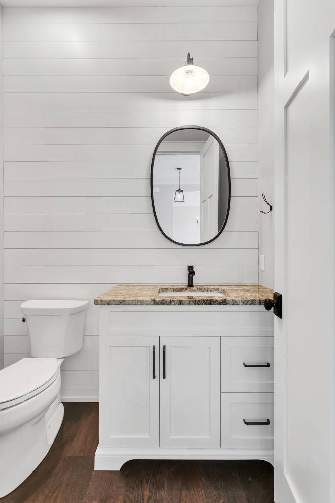 Inredning av ett lantligt mellanstort beige beige toalett, med skåp i shakerstil, vita skåp, en toalettstol med separat cisternkåpa, vit kakel, vita väggar, mörkt trägolv, ett undermonterad handfat, granitbänkskiva och brunt golv