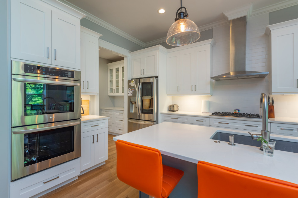 Kitchen - mid-sized transitional l-shaped light wood floor and brown floor kitchen idea with an undermount sink, shaker cabinets, white cabinets, quartzite countertops, white backsplash, ceramic backsplash, stainless steel appliances, an island and white countertops