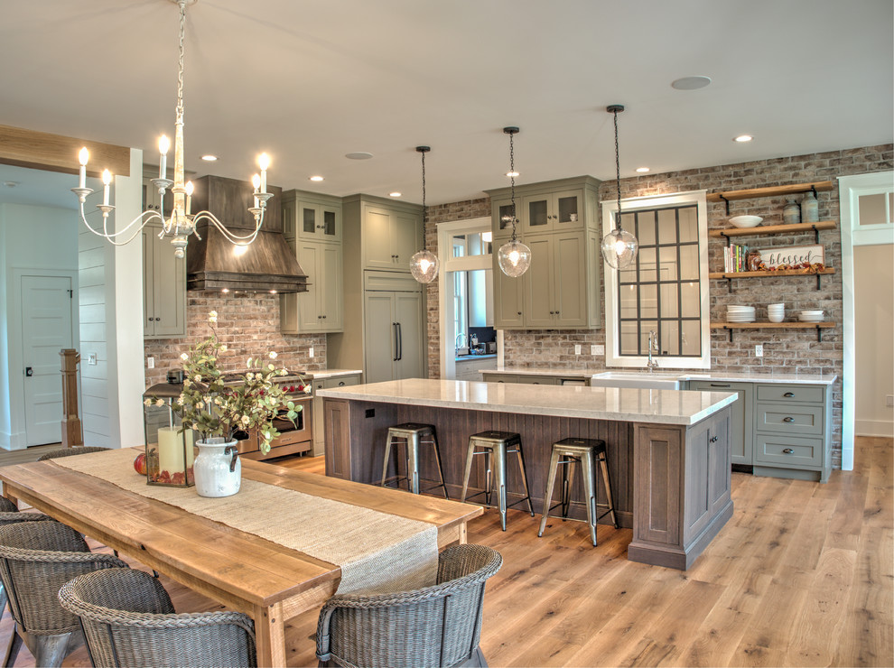 Design ideas for a mid-sized transitional l-shaped open plan kitchen in Philadelphia with a farmhouse sink, shaker cabinets, brick splashback, stainless steel appliances, with island, white benchtop, grey cabinets, quartz benchtops, red splashback, light hardwood floors and beige floor.