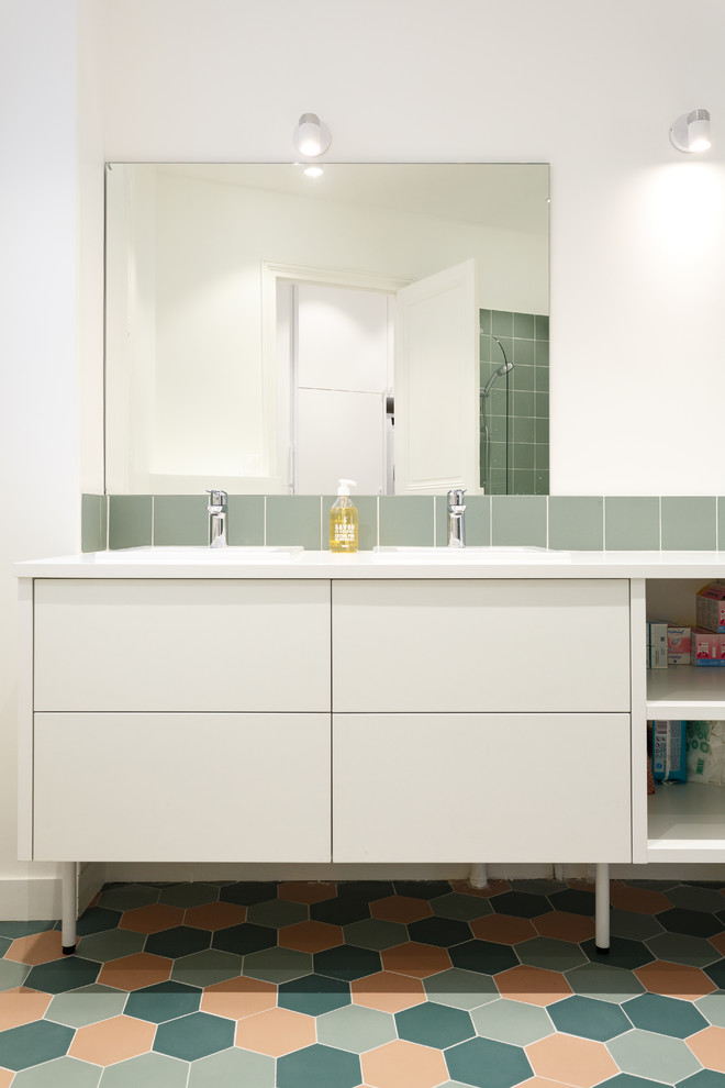 This is an example of a mid-sized modern master bathroom in London with flat-panel cabinets, white cabinets, an undermount tub, a shower/bathtub combo, a two-piece toilet, green tile, ceramic tile, white walls, ceramic floors, a drop-in sink, solid surface benchtops, multi-coloured floor and white benchtops.