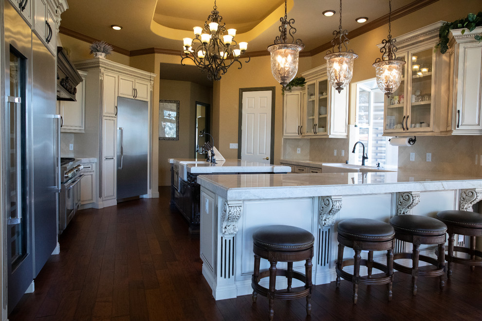 Eat-in kitchen - large mediterranean l-shaped dark wood floor and brown floor eat-in kitchen idea with a farmhouse sink, raised-panel cabinets, distressed cabinets, quartz countertops, beige backsplash, stone tile backsplash, stainless steel appliances, an island and multicolored countertops