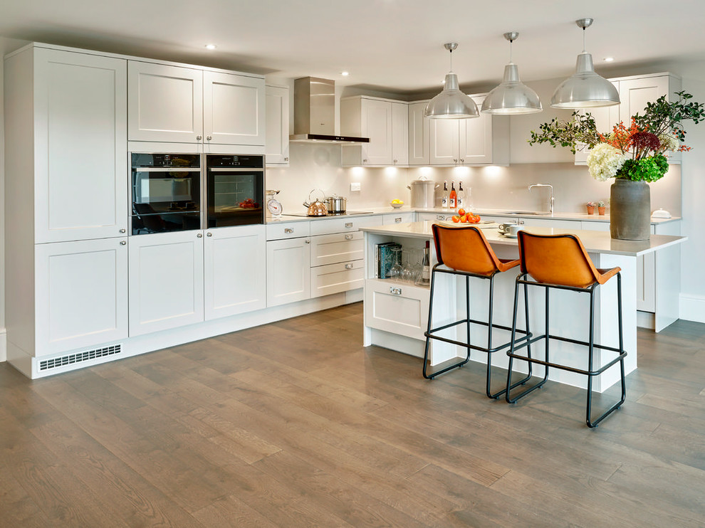 This is an example of a mid-sized transitional kitchen in London with an integrated sink, white splashback, white appliances, painted wood floors, a peninsula and brown floor.