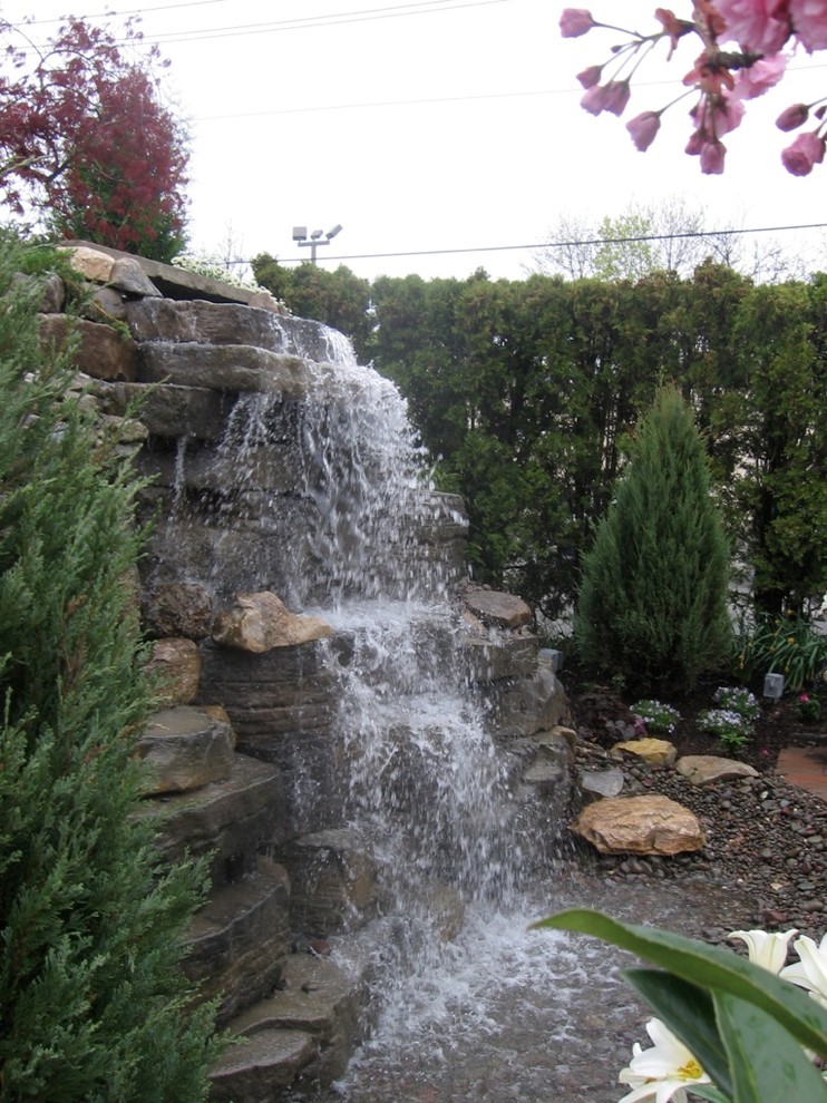 This is an example of a tropical side yard full sun xeriscape for summer in New York with with pond and natural stone pavers.