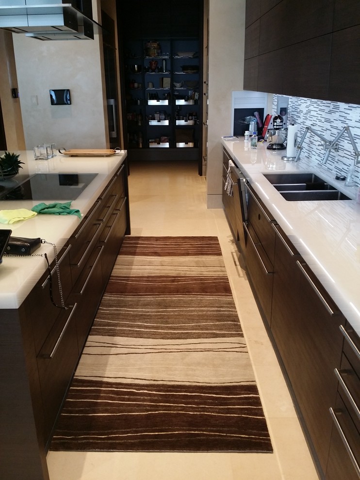 This is an example of a mid-sized contemporary galley open plan kitchen in Seattle with a triple-bowl sink, flat-panel cabinets, dark wood cabinets, solid surface benchtops, multi-coloured splashback, panelled appliances, travertine floors and with island.