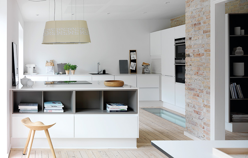 Design ideas for a mid-sized scandinavian u-shaped open plan kitchen in Aarhus with flat-panel cabinets, white cabinets, light hardwood floors, a single-bowl sink, laminate benchtops, black appliances, a peninsula and white benchtop.